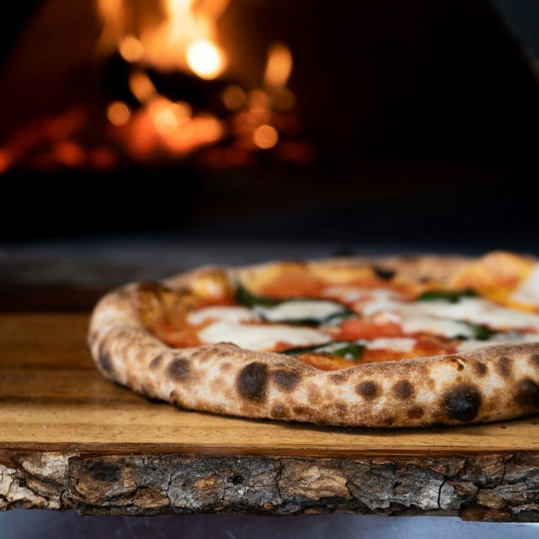Eine Pizza mit Tomatensauce, Mozzarella und frischen Basilikumblättern vor dem Pizzaofen