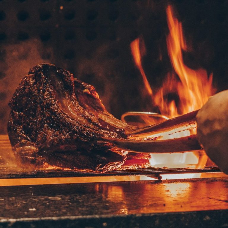 Gegrilltes Fleisch mit Flammen und Holz, das auf einem heißen Grill zubereitet wird.